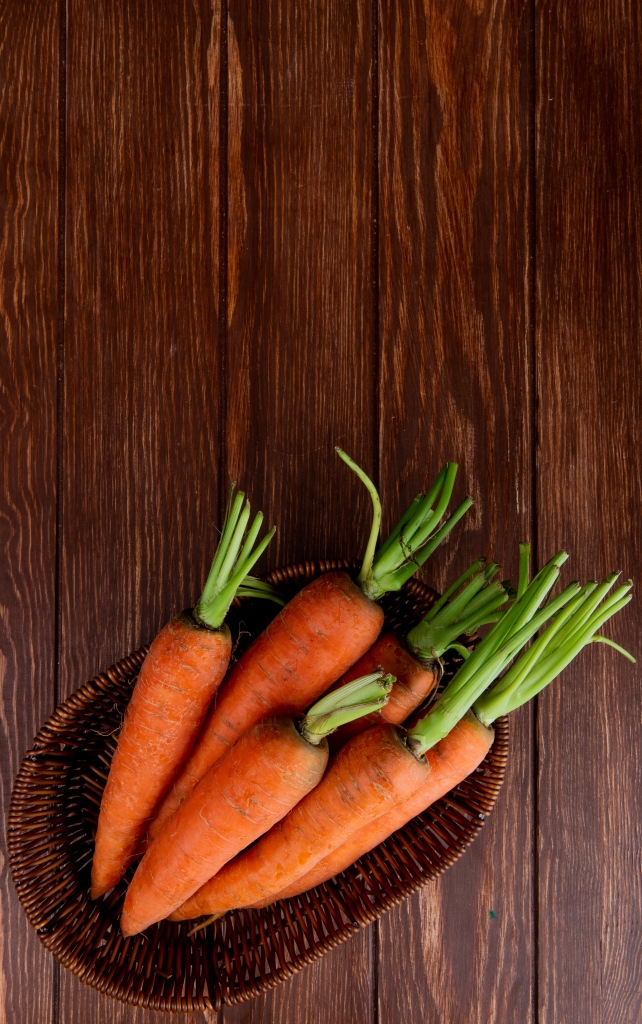 top view of basket plate with carrots on wooden background with copy space